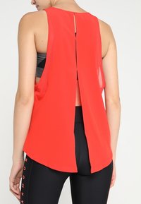 Red sleeveless top with a back slit design, made from lightweight material. Features a rounded hem and layered back for ventilation.