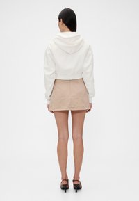 Kurz geschnittener weißer Hoodie mit Kapuze, kombiniert mit einem beigen Minirock. Glatter Stoff, minimalistisches Design und eine klare Silhouette.