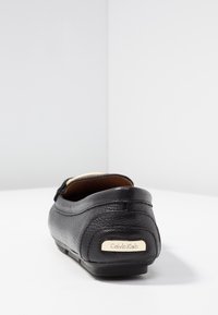 Ballerine plate en cuir noir avec un bout arrondi et une texture subtile. Accessoires dorés avec le logo "Calvin Klein" à l'arrière.