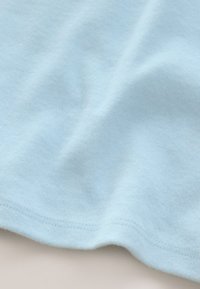 Světle modrá bavlněná látka s hladkou texturou, s jemnými záhyby a prošitým lemem podél spodního okraje.