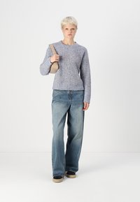 Light blue textured knit sweater with a crew neckline, paired with faded blue wide-leg jeans. Model holds a beige handbag.