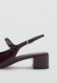 Kengurun dengan tumit tinggi dalam kulit paten burgundy tua, menampilkan tali yang boleh disesuaikan dengan gesper emas dan reka bentuk tumit blok.