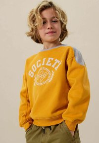 Sweatshirt jaune avec impression blanche "SOCIETA" et détails décoratifs. Accents d'épaule gris. Tissu doux avec une coupe décontractée et des poignets côtelés.