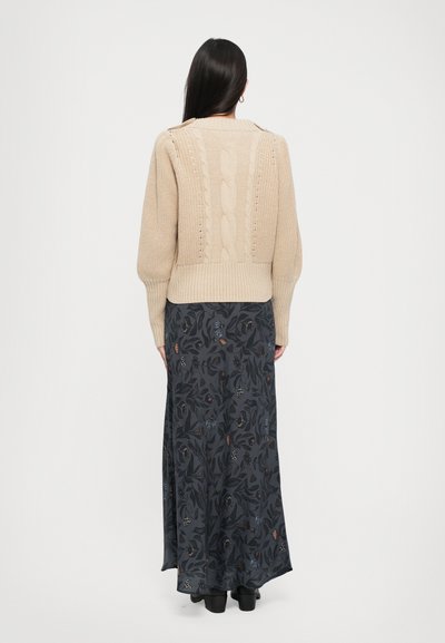 Beige cable-knit sweater with a crew neck, featuring textured patterns, paired with a long dark floral skirt and black ankle boots.