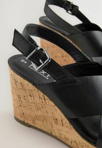 Black leather wedge sandals with a cork base, featuring adjustable ankle straps and a silver buckle detail.