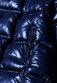 Chaqueta puffy azul marino con tela brillante y acolchada, y costuras pronunciadas. Presenta grandes secciones aisladas con una textura suave.