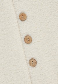White textured fabric with three wooden buttons. The surface appears fuzzy, adding a soft tactile quality to the overall design.