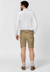 Beige Leder-Shorts mit glatter Textur, ausgestattet mit Seitentaschen und einem Gürtel. Kombiniert mit einem weißen Hemd und braunen Schuhen.