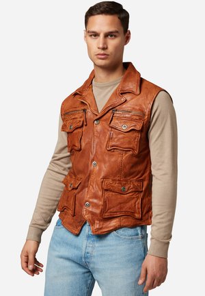 Brun lædervest med flere frontlommer, krave og knaplukninger. Bæres over en beige langærmet skjorte.