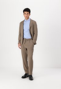 Beige dressjakke med slim fit, parret med en lyseblå skjorte med knapper. Bukserne har elastisk linning og bæres med sorte sko.