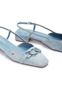 Chaussures slingback en daim bleu clair avec un bout carré, un petit talon et un détail de chaîne décoratif. Présente une finition souple et texturée.