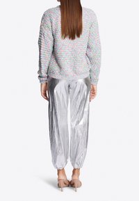 Pastel-colored, textured sweater with a round neckline paired with shiny, silver, pleated pants featuring elastic cuffs. Neutral-toned heels.
