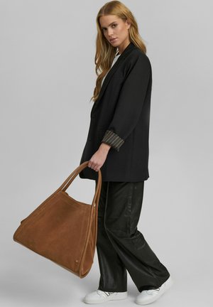Schwarzer oversized Blazer mit gestreiften Manschetten, kombiniert mit lockeren schwarzen Hosen und einer großen braunen Wildleder-Tote. Weiße Sneakers runden den Look ab.
