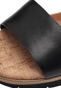 Sandale à glissière en cuir noir avec une large bandoulière, semelle en liège et semelle extérieure texturée. Présente un motif de grain de bois naturel.