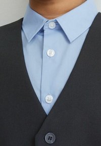Dark vest over light blue collared shirt with two white buttons, featuring a sharp collar and smooth fabric texture.