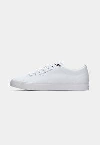 Baskets blanches basses avec bout rond, lacets à l'avant, semelle plate et logo Tommy Hilfiger sur le côté et près des lacets.