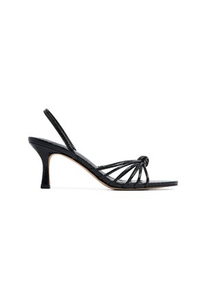 Black leather heeled sandal with multiple thin straps, a knotted detail at the front, and a slender heel. Smooth texture and minimalist design.