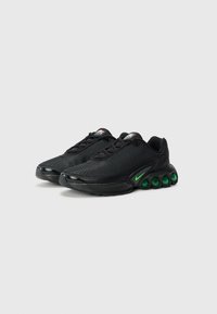Black athletic shoes with a mesh upper, green accents on the sole, and a distinctive rounded heel design. Features a lace-up closure.