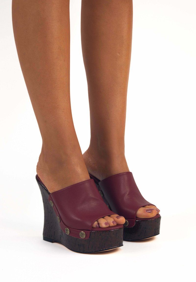 Sandali wedge a punta aperta bordeaux con una piattaforma in legno testurizzata e borchie metalliche decorative. Parte superiore in sintetico liscia con un design semplice.