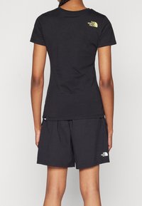 Černé tričko s krátkým rukávem a žlutým logem na horní části zad, doplněné o černé šortky se shodným designem a bílým logem na boku.