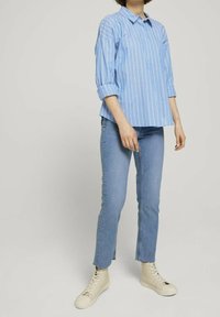 Ljusblå randig skjorta med uppvikta ärmar, i kombination med ljusblå jeans och krämfärgade högstövlar. Avslappnad, lös passform.