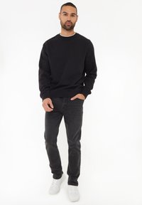 Czarna bluza z okrągłym dekoltem, noszona z ciemnymi dżinsami i białymi sneakersami. Bluza ma długie rękawy i luźny krój.