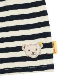 Tejido a rayas que presenta franjas alternas en azul marino y crema, con un aplique texturizado de un oso en un color claro en el lateral.