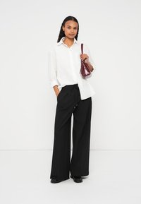 Valge nööbitav särk, mustad laiad püksid ja väike burgundia käekott. Sile kangas ja lõdva lõikega. Mustad kingad läikiva viimistlusega.