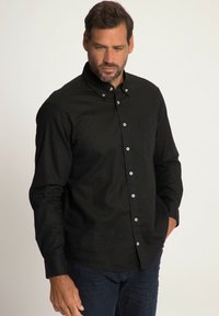 Camisa negra de botones con mangas largas, un bolsillo en el pecho y botones blancos. La tela parece suave con una textura sutil. Combina con jeans oscuros.
