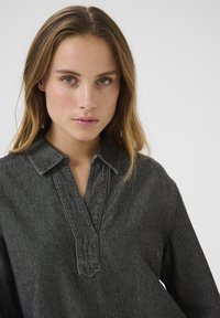 Sort denimskjorte med krave, knaplukning og lange ærmer. Har et tekstureret stof og subtile syninger.