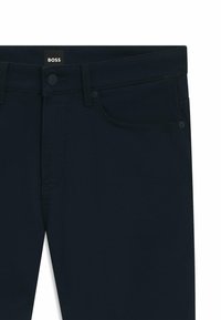 Pantaloni blu scuro con bottone anteriore, passanti per cintura e tasche frontali, dotati di una piccola etichetta "BOSS" nella cintura.