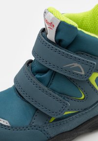 Wysokie buty dziecięce w kolorze niebieskim i neonowo-żółtym. Wyposażone w dwie regulowane zapięcia na rzepy, teksturowaną tkaninę oraz gumową podeszwę zapewniającą przyczepność.