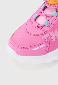 Zapatilla rosa con suela blanca, ojales azules para los cordones y texto "Looney Tunes" en el lateral cerca de la punta, sobre un fondo blanco.