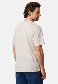 Cremefarvet kortærmet t-shirt med rund hals, lavet af blødt stof, der har en afslappet pasform og synlige syninger.