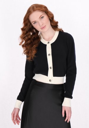 Černý zkrácený cardigan s krémovými manžetami a léga, s velkými černými knoflíky. Hladká textura, ribovaný design a přiléhavý styl.