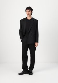 Black tailored suit featuring a double-breasted blazer and straight-leg trousers, worn over a black shirt, completed with black dress shoes.