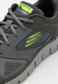 Grau gestrickter und synthetischer Sneaker mit leichtem Design, ausgestattet mit einem grünen Logo und strukturierten Akzenten an den Seiten und der Sohle.