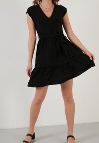 Svart kort klänning med v-ringning, korta ärmar och cinchad midja. Har en utsvängd kjol och en texturerad väv. Bärs med svarta klacksandaler.