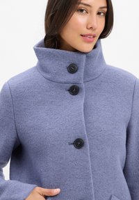 Hellblauer Wollmantel mit hohem Kragen, drei schwarzen Knöpfen und einer weichen Textur. Verfügt über seitliche Taschen und ein lässiges Design.