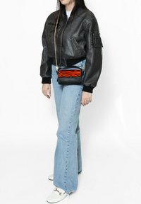 Giubbotto bomber in pelle nera, jeans a zampa d'elefante di colore blu chiaro e una piccola borsa a tracolla nera con un motivo a strisce zebra arancioni. Scarpe bianche.