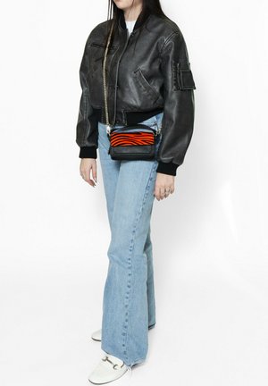 Schwarze Leder-Bomberjacke, hellblaue Schlagjeans und eine kleine schwarze Crossbody-Tasche mit einem orangefarbenen Zebra-Streifenmuster. Weiße Schuhe.