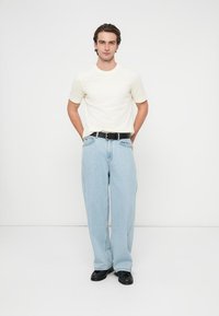 Biała koszulka z krótkim rękawem, jasnoniebieskie szerokie dżinsy, czarny pasek i czarne buty. Prosty design, casualowy krój, gładka faktura.