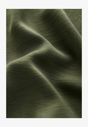 Tissu olive vert texturé drapé en plis, mettant en valeur des motifs de vagues subtils et une surface douce et lisse. Matériau léger et flexible.