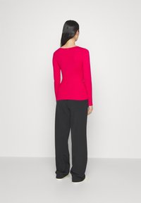 Top aderente a maniche lunghe di un vivace colore rosa, con un ampio scollo e trama a coste. Abbinato a pantaloni neri larghi e scarpe di colore chiaro.