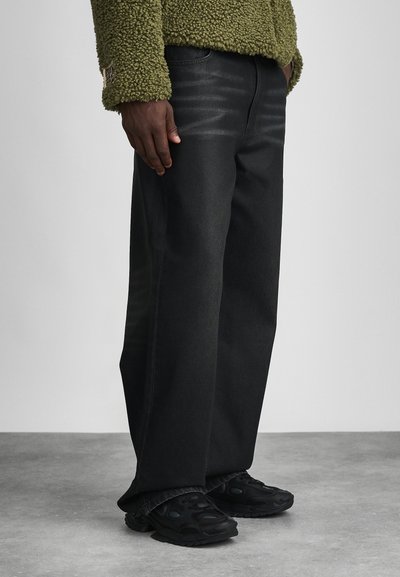 Jeans in denim nero con una vestibilità ampia, caratterizzati da leggeri effetti di usura e gamba dritta. Abbinati a un pile testurizzato color verde oliva e sneakers nere.