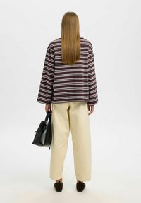 Triibulise pruunvalge pika varrukaga pluus, kreemikas laiade sääreosadega püksid, must käekott ja tumedad kingad. Juuksed on sirged ja langevad seljale.