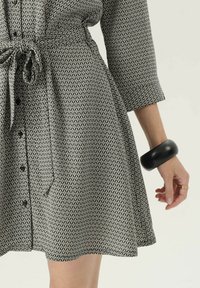 Czarna i biała sukienka w wzory w luźnym kroju, z buttonami z przodu i paskiem w talii. Posiada geometryczny wzór w diamenty oraz rękawy o długości trzech czwartych.
