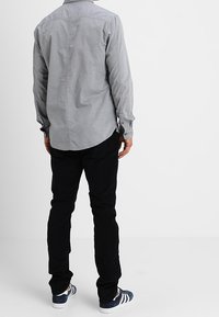 Chemise grise boutonnée, tissu en coton, manches longues. Pantalon noir, coupe slim. Baskets bleues avec des rayures blanches. Construction simple, sans motifs.