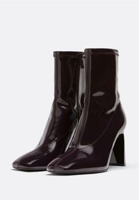 Burgundi patento ankle boots dengan ujung runcing, ritsleting samping, dan tumit persegi tinggi. Memiliki jahitan yang terlihat di sepanjang tepi atas.