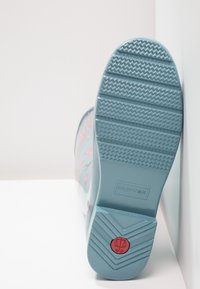 Bota de goma azul con patrón floral, suela texturizada y logo circular rojo en el talón. Presenta un material suave y diseño de punta redondeada.